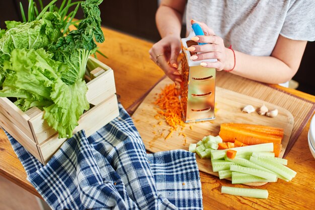 Woman grates the carrots on a wooden board