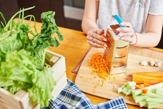 Woman grates the carrots on a wooden board