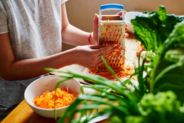 Woman grates the carrots on a wooden board