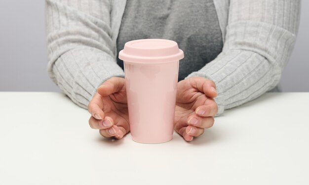 Женщина в серой одежде держит розовую керамическую чашку, женщина сидит за белым столом, начало дня, утро