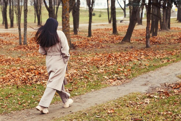 秋の公園を歩いている灰色のコートを着た女性