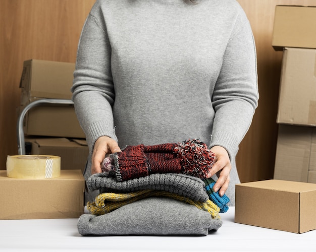 La donna in un maglione grigio raccoglie i vestiti in una scatola, concetto di assistenza e volontariato, spostamento. vendere cose inutili