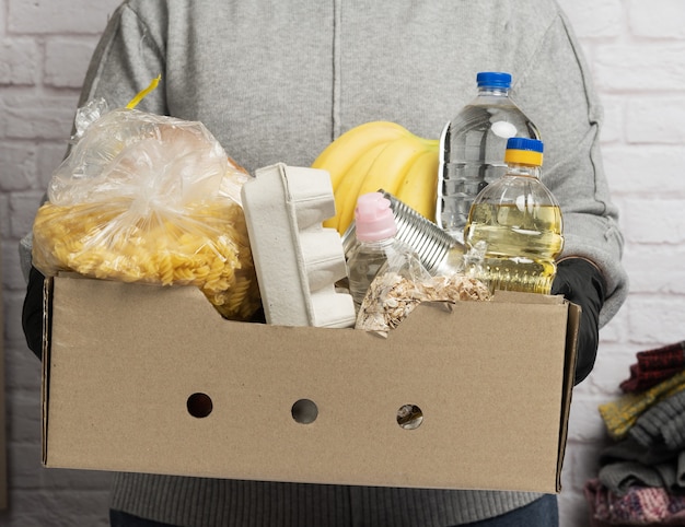 Woman in a gray sweater is packing food in a cardboard box, the concept of assistance and volunteering, donation