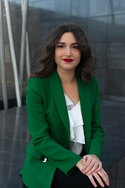 A woman in a green blazer sits on a bench.