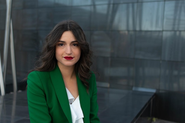 A woman in a green blazer stands in front of a black wall.