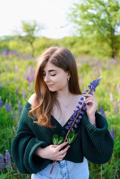 Photo a woman in a green blouse holding a lupine flower in a field