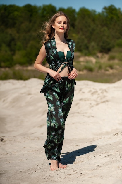 A woman in a green camouflage jumpsuit stands on a sandy beach.