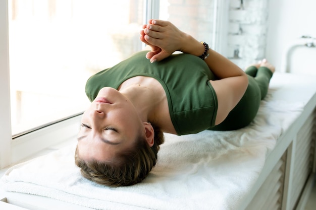 Woman in green closes, lying on her back, palms connected on chest, doing mental practice and relaxation