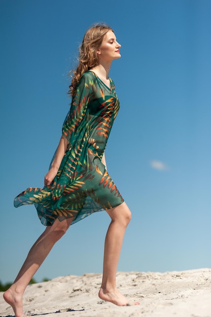 A woman in a green dress is walking on a beach.