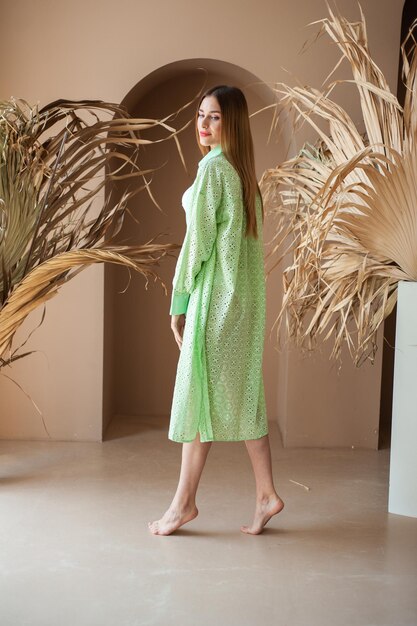 A woman in a green dress stands in front of a wall with plants