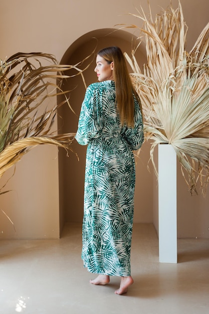 A woman in a green palm leaf dress stands in a white room