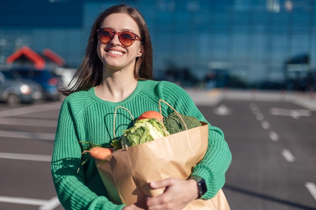 Woman in green sweater holding paper bag with full of groceries in hands