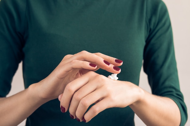 Woman in a green T-shirt and a maroon manicure applying hand cream