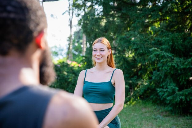 A woman in a green tank top is smiling during a fitness class in the outdoors