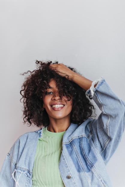 Woman in green tshirt ruffles hair on white background Pretty girl in denim jacket and tee smiling and posing on isolated backdrop