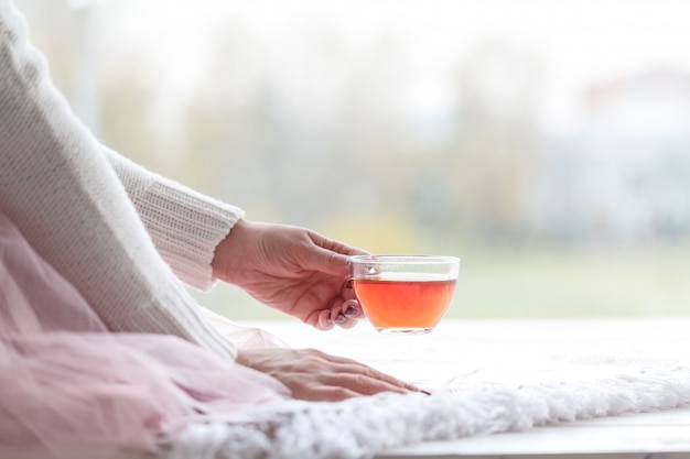 Foto donna in un maglione grigio che tiene una tazza di tè mentre era seduto su una coperta a maglia bianca