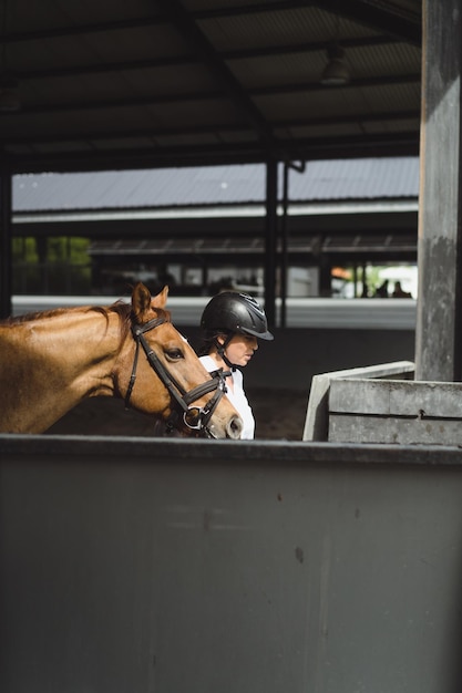 女性グルーマーは、競馬場での授業の後、馬のひづめを洗います。女性は馬の世話をし、訓練後に馬を洗います。