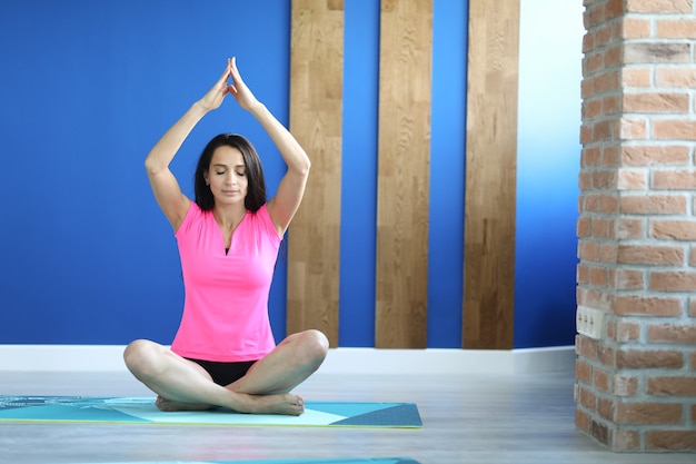 Woman in gym sits in lotus position with her eyes closed.