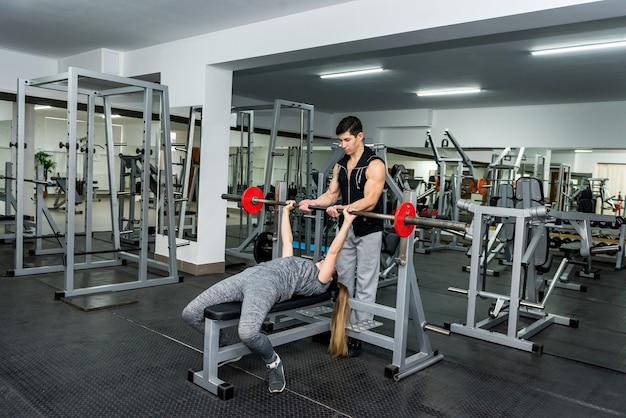 Donna in palestra che lavora con il bilanciere con l'aiuto dell'istruttore