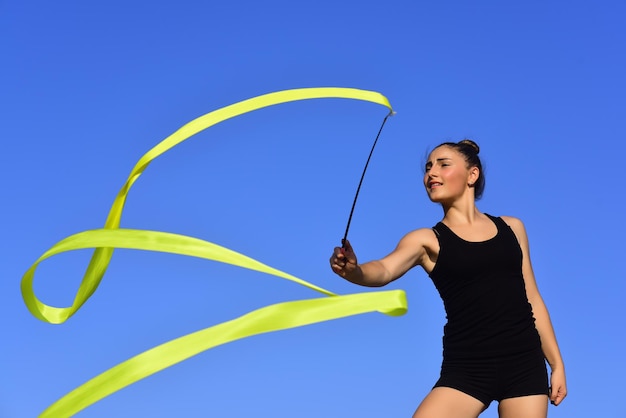 Woman gymnast in black sportswear with green ribbon.