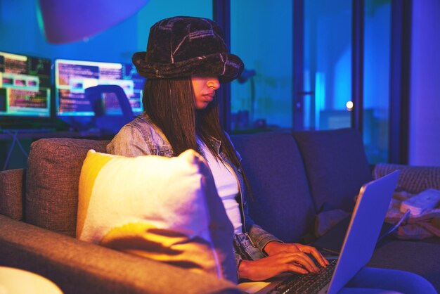 Photo woman hacker and programmer typing on laptop in home at night in neon to hack software cybersecurity sofa ransomware phishing and female coder coding on computer for hacking database with malware