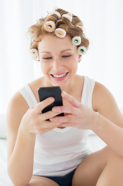 Woman in hair curlers text messaging on bed