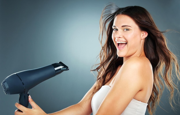 Photo woman hair and hair dryer with smile in studio for self care hair care or cosmetics by blue background girl happy and excited with hairdryer for wellness cosmetic care and beauty by backdrop