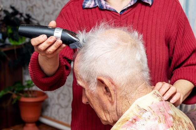 Woman haircut an elderly man with a trimmer Haircut at home