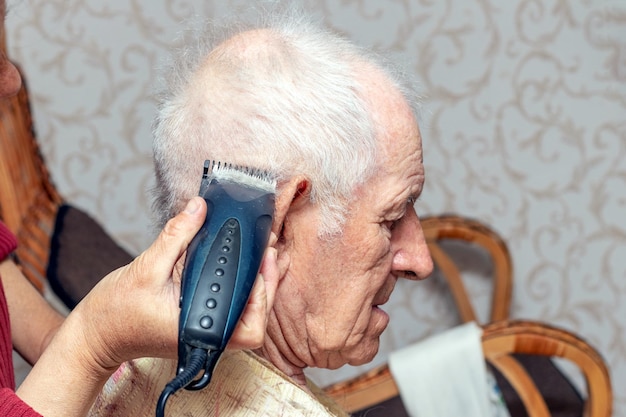 Woman haircut an elderly man with a trimmer Haircut at home