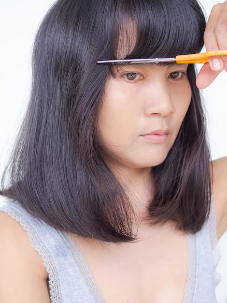 woman haircutting with scissors at home on white background. styling fashion. portrait authentic black hair, skin tan and slim fit asian thailand lady. life style for beauty and good health.