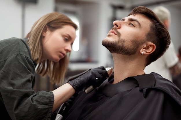 Woman hairdresser cut beard handsome caucasian young man