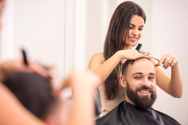 Женщина-парикмахер стрижет мужчине волосы.
