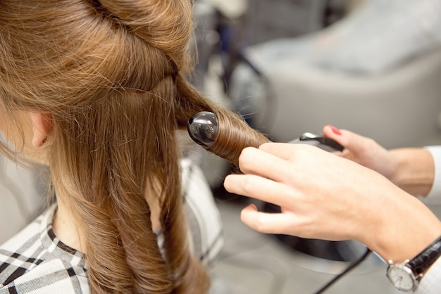 ビューティーサロンでブロンドの女の子に髪型を作る女性美容師。