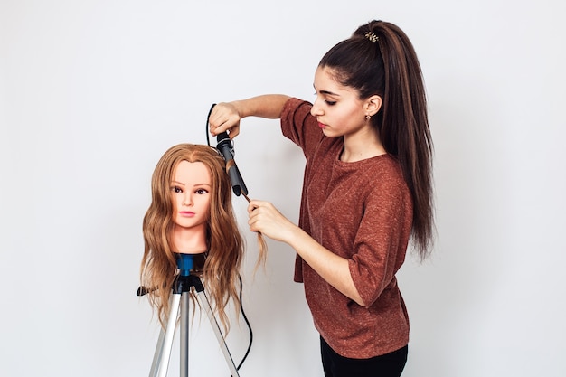 Woman hairdresser student studying on mannequin head.