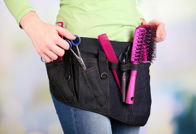 Woman hairdresser with tool belt on bright background