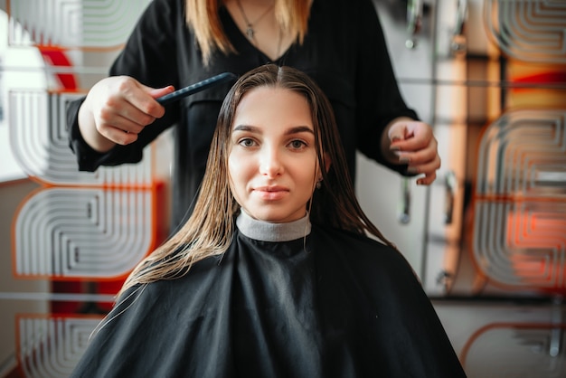 Woman in hairdressing salon, female stylist with scissors and comb in hands. Hairstyle making in beauty salon