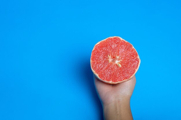 Woman han holding a cut pink grapefruit isolated on blue background Citrus isolated