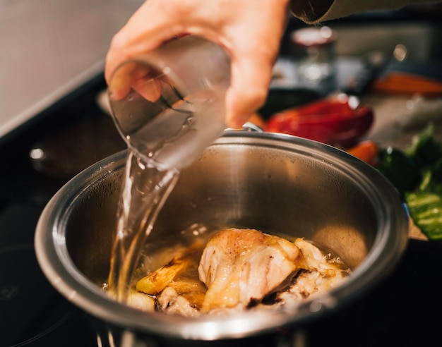 Рука женщины добавляет воду в кастрюлю Готовит куриный суп