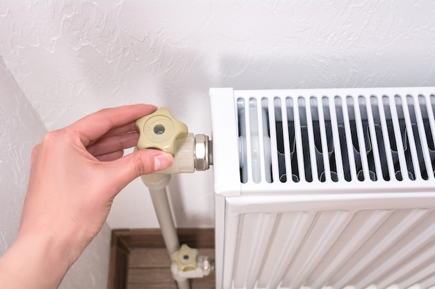 Woman hand adjusting the knob of heating radiator. Expensive heating costs concept