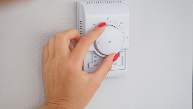 여자 손으로 벽 온도 컨트롤러 컨트롤러 버튼을 조정하거나 켭니다.