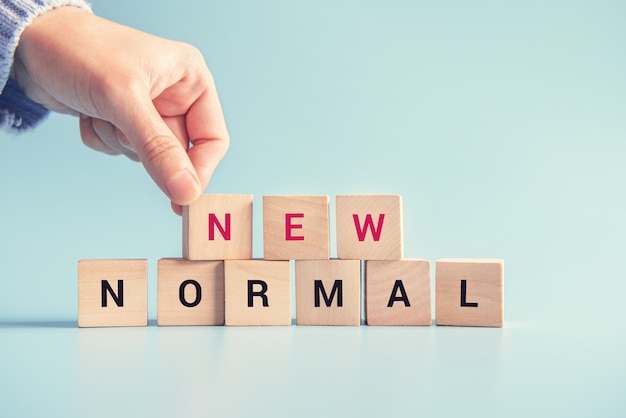 Woman hand arranging wooden cubes with NEW NORMAL word