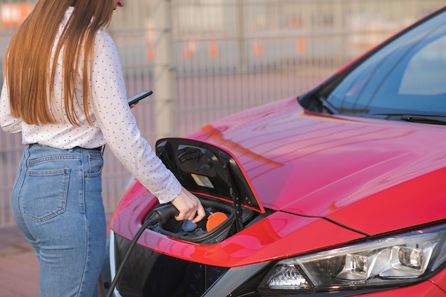 環境に優しいゼロエミッション電気自動車に電源ケーブルを接続する女性の手。女性は充電されている電気自動車に接続されている電源を作ります。