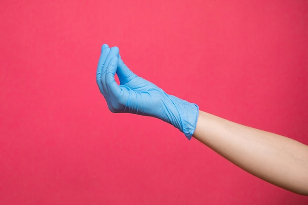 Woman hand in blue medical glove pretending to hold medicine on pink background