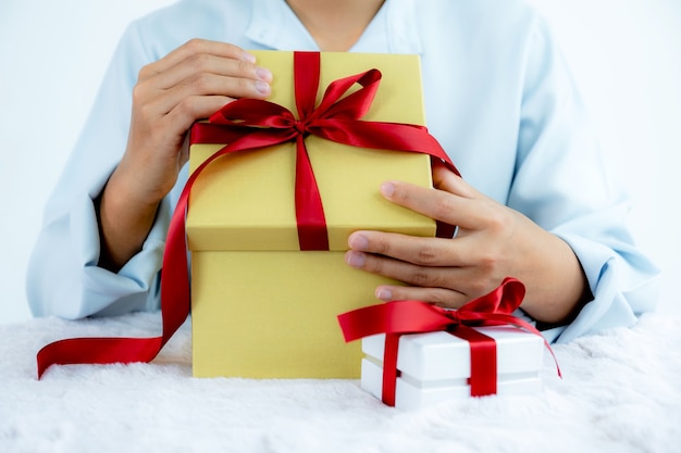 Woman hand in a blue shirt opening a gold gift box tied with a red ribbon present for the festival of giving special holidays like Christmas, Valentine's Day.