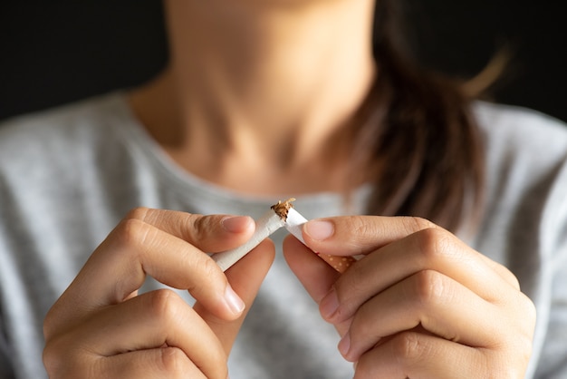 Woman hand breaking, crushing or destroying cigarettes on black background.