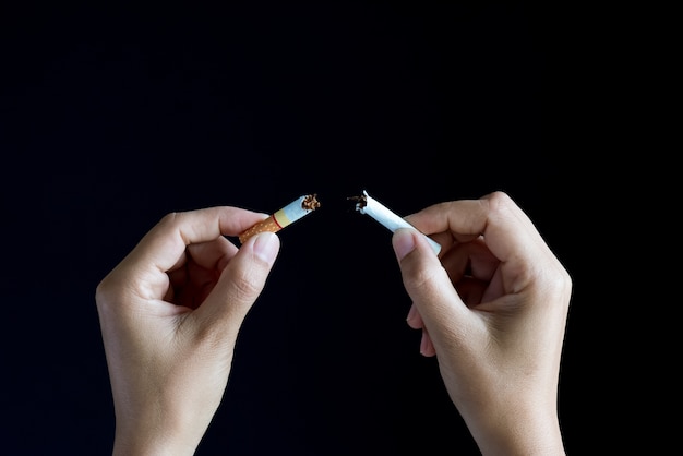 Woman hand breaking, crushing or destroying cigarettes on black background.