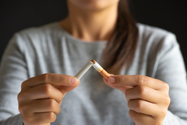 woman hand breaking, crushing or destroying cigarettes on black background.