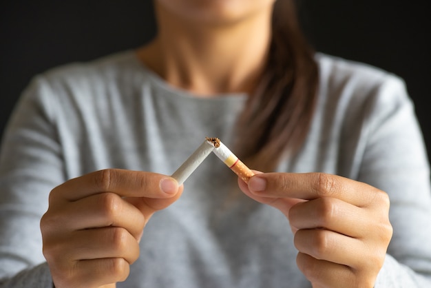 Woman hand breaking, crushing or destroying cigarettes on black background.