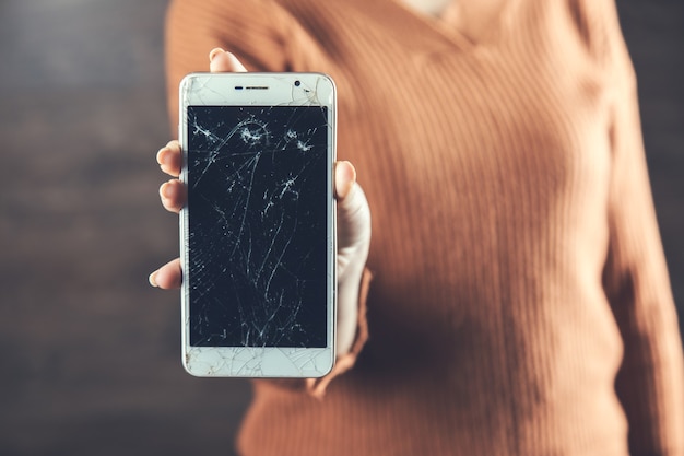 Woman hand broken smart phone on dark