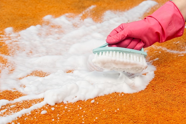 Foto macchia di pulizia della mano della donna sulla moquette con la spazzola dura. close up di pulizia a umido tappeto arancione. concetto di servizio di pulizia della moquette